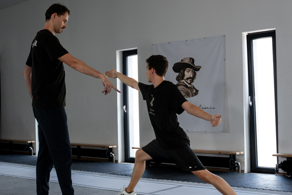 men doing a fencing lunge and coach correcting him